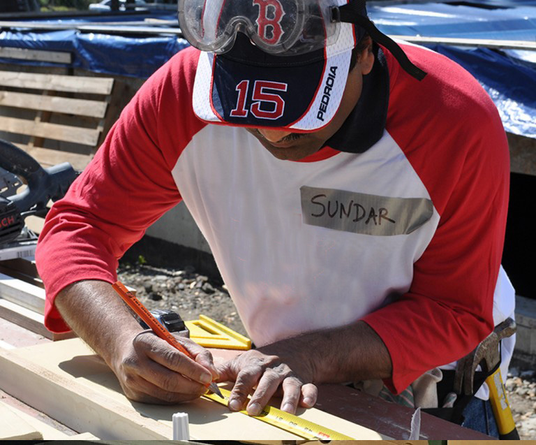 Sundar, a Seedvester using a tape measure while volunterring in his BBH Cares t-shirt and Red Sox hat with safety goggles on his head. 